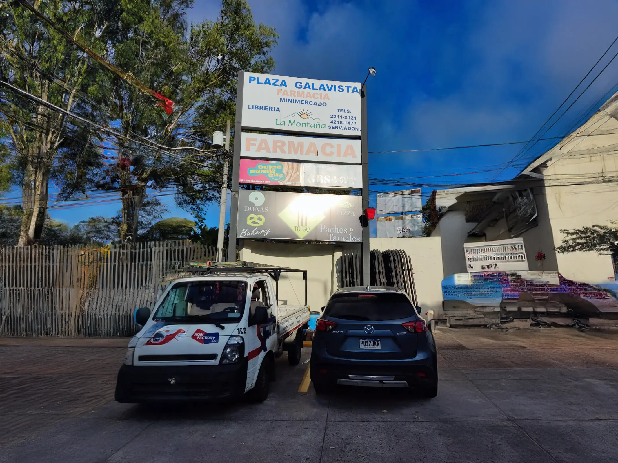 Tótem exterior iluminado con tiendas como una farmacia, un salón de belleza y una pizzería.