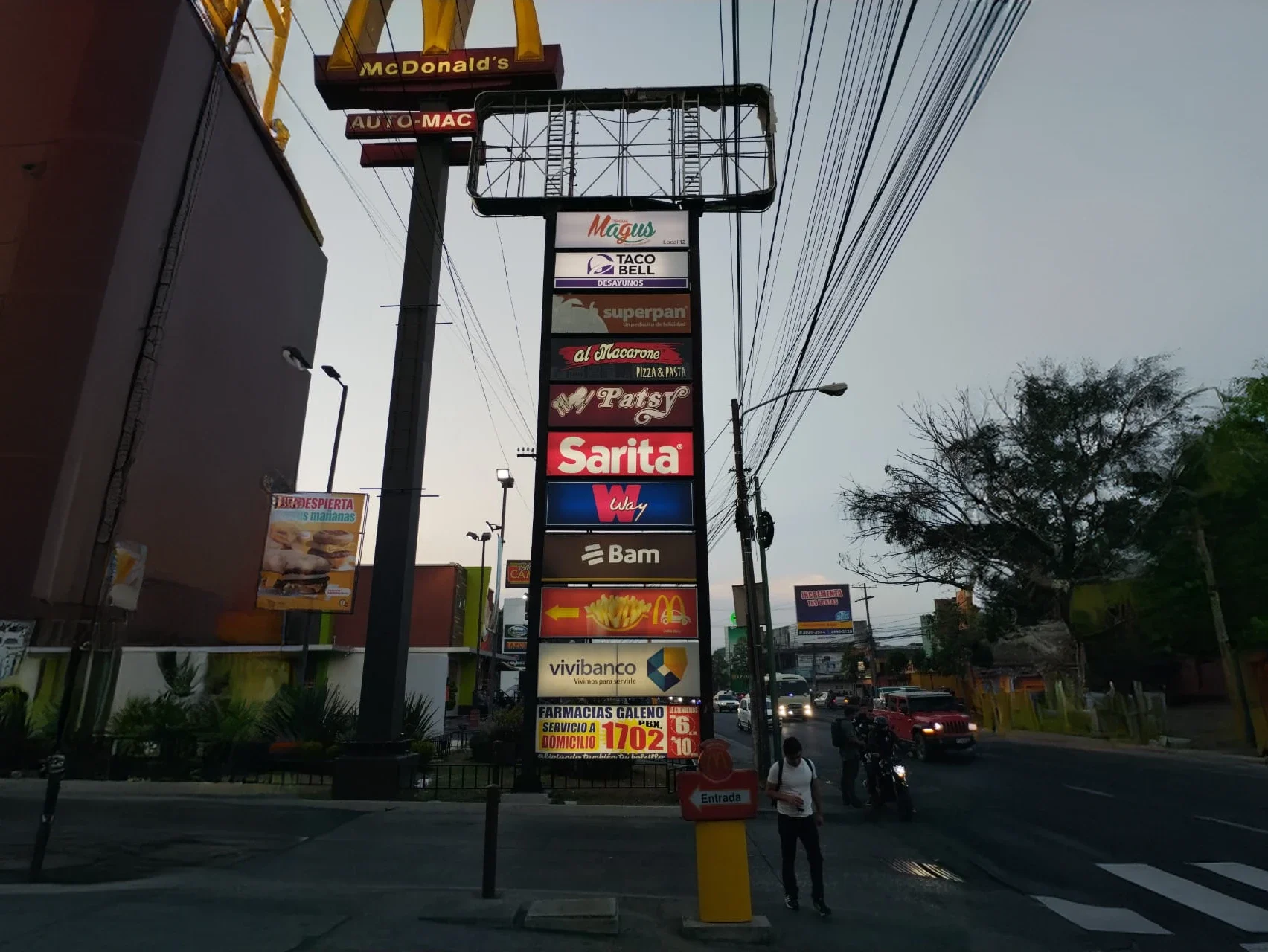 Tótem exterior iluminado con tiendas como Magus, Taco Bell, Super Pan, Al macarone, Patsy, Sarita, Way, Bam, Vivibanco y Farmacias Galeno.